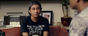 Movie still from “Dope” (2015), directed by Rick Famuyiwa – A young man wearing a hat sitting on a couch in a living room; Close Up shot, Over the shoulder angle