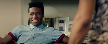 Movie still from “Dope” (2015), directed by Rick Famuyiwa – A young man smiles for the camera in a living room; Close Up shot, Over the shoulder angle