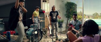 Movie still from “Dope” (2015), directed by Rick Famuyiwa – A group of young men playing instruments in front of a microphone; Wide shot, High angle