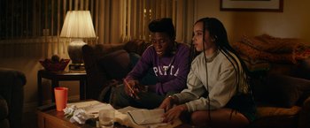 Movie still from “Dope” (2015), directed by Rick Famuyiwa – Two people sitting on a couch looking at papers; Medium shot, Over the shoulder angle