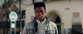 Movie still from “Dope” (2015), directed by Rick Famuyiwa – A person with a microphone in front of a building; Close Up shot, Low angle