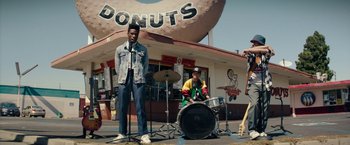 Movie still from “Dope” (2015), directed by Rick Famuyiwa – A man and a woman playing drums in front of a donut shop; Wide shot, Low angle
