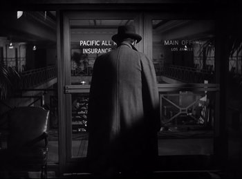 Movie still from “Double Indemnity” (1944), directed by Billy Wilder – A man wearing a coat and a hat standing in front of a building; Wide shot, High angle