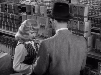 Movie still from “Double Indemnity” (1944), directed by Billy Wilder – A man and a woman are standing in front of boxes; Medium shot, Over the shoulder angle