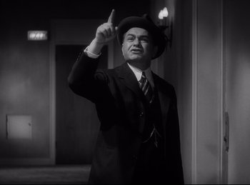 Movie still from “Double Indemnity” (1944), directed by Billy Wilder – A man in a suit and hat is pointing up; Medium shot, Low angle