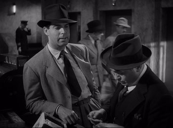 Movie still from “Double Indemnity” (1944), directed by Billy Wilder – A man in a suit and tie standing next to another man in a hat; Medium shot, Low angle