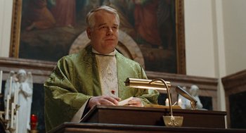 Movie still from “Doubt” (2008), directed by John Patrick Shanley – A man in a priest's outfit sitting in front of a microphone; Medium shot, Low angle