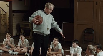 Movie still from “Doubt” (2008), directed by John Patrick Shanley – A man holding a basketball in front of a group of kids; Medium shot, Over the shoulder angle