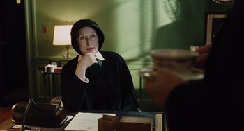 Movie still from “Doubt” (2008), directed by John Patrick Shanley – A person sitting at a table wearing a robe; Medium shot, Over the shoulder angle
