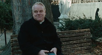 Movie still from “Doubt” (2008), directed by John Patrick Shanley – A priest sitting on a park bench in front of a statue; Close Up shot, Over the shoulder angle