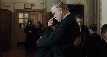 Movie still from “Doubt” (2008), directed by John Patrick Shanley – Two men in suits hugging each other in front of a group of people; Close Up shot, Over the shoulder angle