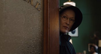 Movie still from “Doubt” (2008), directed by John Patrick Shanley – An older woman wearing glasses and a hat looking over a wall; Medium shot, Over the shoulder angle