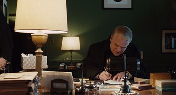 Movie still from “Doubt” (2008), directed by John Patrick Shanley – A man sitting at a desk writing on a piece of paper; Medium shot, Over the shoulder angle