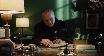 Movie still from “Doubt” (2008), directed by John Patrick Shanley – A man sitting at a desk reading a book; Medium shot, Over the shoulder angle
