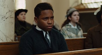 Movie still from “Doubt” (2008), directed by John Patrick Shanley – A man sitting in front of a group of people in a room; Close Up shot, Low angle