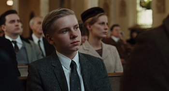 Movie still from “Doubt” (2008), directed by John Patrick Shanley – A man in a suit and tie sitting in front of other people; Close Up shot, Over the shoulder angle
