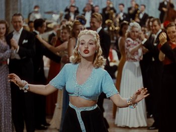 Movie still from “Down Argentine Way” (1940), directed by Irving Cummings – A woman in a blue top is dancing in a crowd of people; Medium shot, Low angle