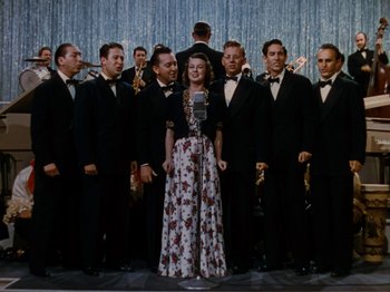 Movie still from “Down Argentine Way” (1940), directed by Irving Cummings – A group of men and a woman standing next to each other in front of a microphone; Wide shot, High angle