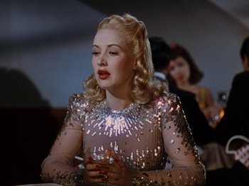 Movie still from “Down Argentine Way” (1940), directed by Irving Cummings – A woman in a silver dress holding a drink; Medium shot, Over the shoulder angle