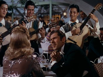 Movie still from “Down Argentine Way” (1940), directed by Irving Cummings – A group of people sitting at a table with guitars; Medium shot, Over the shoulder angle