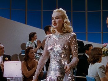 Movie still from “Down Argentine Way” (1940), directed by Irving Cummings – A woman in a silver dress standing in front of a group of people; Medium shot, Low angle