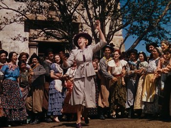 Movie still from “Down Argentine Way” (1940), directed by Irving Cummings – An older woman in a hat and a long dress is dancing with a group of people in the background; Wide shot, Low angle
