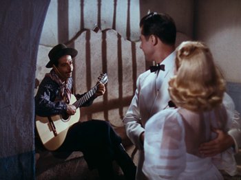 Movie still from “Down Argentine Way” (1940), directed by Irving Cummings – A man playing a guitar while two other people watch; Wide shot, High angle