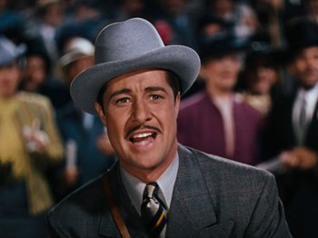 Movie still from “Down Argentine Way” (1940), directed by Irving Cummings – A man in a suit and a hat is standing in front of a crowd; Close Up shot, High angle