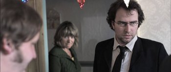 Movie still from “Down Terrace” (2009), directed by Ben Wheatley – A man and a woman standing next to each other in a room; Close Up shot, Over the shoulder angle