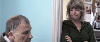 Movie still from “Down Terrace” (2009), directed by Ben Wheatley – A woman standing in front of a man in a room; Close Up shot, Over the shoulder angle