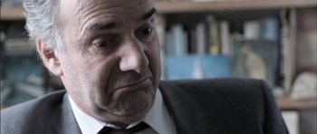 Movie still from “Down Terrace” (2009), directed by Ben Wheatley – An older man wearing a suit and tie looking sad; Close Up shot, Over the shoulder angle