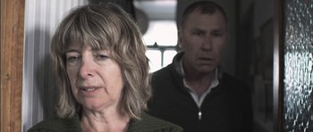 Movie still from “Down Terrace” (2009), directed by Ben Wheatley – An older woman and a younger man in the background; Close Up shot, Over the shoulder angle