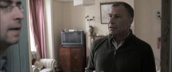 Movie still from “Down Terrace” (2009), directed by Ben Wheatley – A person standing in a living room; Close Up shot, Over the shoulder angle