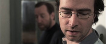 Movie still from “Down Terrace” (2009), directed by Ben Wheatley – A man with glasses is looking at the camera; Close Up shot, Over the shoulder angle