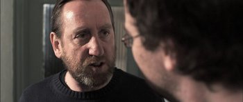 Movie still from “Down Terrace” (2009), directed by Ben Wheatley – A man with a goatee talking to another man; Close Up shot, Over the shoulder angle