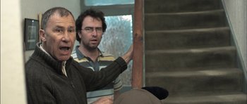 Movie still from “Down Terrace” (2009), directed by Ben Wheatley – Two men standing next to each other in front of a staircase; Medium shot, Over the shoulder angle