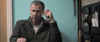 Movie still from “Down Terrace” (2009), directed by Ben Wheatley – A man holding a cell phone up to his ear; Close Up shot, Low angle