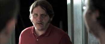 Movie still from “Down Terrace” (2009), directed by Ben Wheatley – A person wearing a red shirt; Close Up shot, Low angle