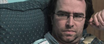 Movie still from “Down Terrace” (2009), directed by Ben Wheatley – A person wearing glasses on a couch; Close Up shot, Over the shoulder angle