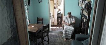 Movie still from “Down Terrace” (2009), directed by Ben Wheatley – A man sitting on a chair in a room with blue walls; Wide shot, Low angle
