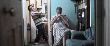 Movie still from “Down Terrace” (2009), directed by Ben Wheatley – A man sitting in a chair in front of another man; Medium shot, Low angle