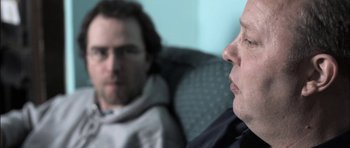 Movie still from “Down Terrace” (2009), directed by Ben Wheatley – Two men are sitting in a chair and one is looking at the camera; Close Up shot, Over the shoulder angle