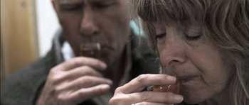 Movie still from “Down Terrace” (2009), directed by Ben Wheatley – A man and a woman are eating a donut; Extreme Close Up shot, Over the shoulder angle