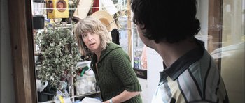 Movie still from “Down Terrace” (2009), directed by Ben Wheatley – A woman in a green sweater talking to a man in a straw hat; Medium shot, Over the shoulder angle