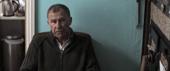 Movie still from “Down Terrace” (2009), directed by Ben Wheatley – An older man sitting in front of a blue wall; Close Up shot, Low angle