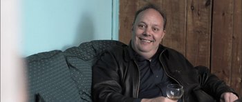Movie still from “Down Terrace” (2009), directed by Ben Wheatley – A man sitting on a couch holding a glass of wine; Close Up shot, Over the shoulder angle