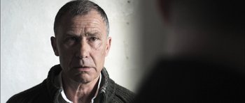 Movie still from “Down Terrace” (2009), directed by Ben Wheatley – An older man looking into a mirror with a serious look on his face; Close Up shot, Over the shoulder angle