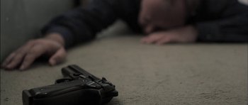 Movie still from “Down Terrace” (2009), directed by Ben Wheatley – A man laying on the ground next to a gun; Extreme Close Up shot, Overhead angle