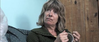 Movie still from “Down Terrace” (2009), directed by Ben Wheatley – An older woman is looking at the camera; Close Up shot, Over the shoulder angle