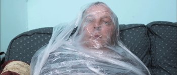 Movie still from “Down Terrace” (2009), directed by Ben Wheatley – A man wrapped in plastic looking at the camera; Close Up shot, Overhead angle